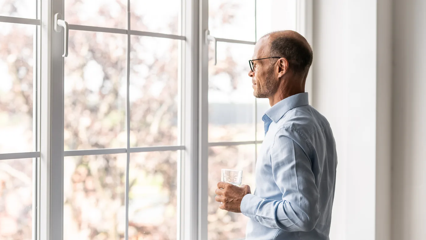 Mann am Fenster mit Glas Wasser